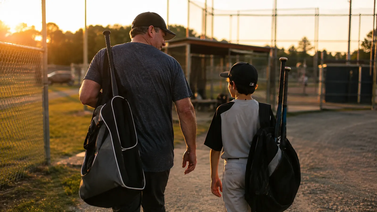 A bat rack and a broken-in fielding glove on a dugout bench in late afternoon light